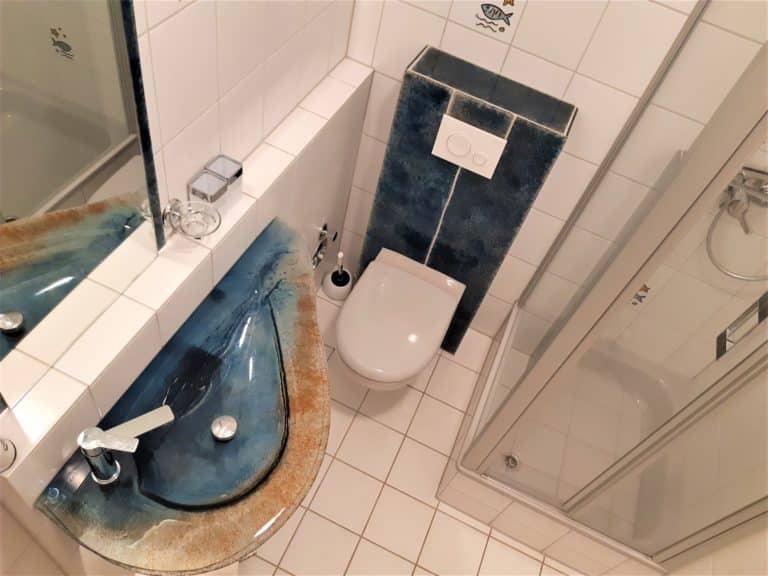 20220625_154358 (2) – Hubertus Boltenhagen Kleines Badezimmer mit Dusche, WC und blauem Waschbecken.
