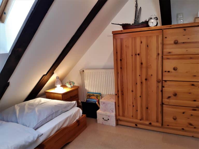 20220625_163145 (2) – Hubertus Boltenhagen Gemütliches Schlafzimmer mit Holzschrank und Einzelbett unter Schrägdach.