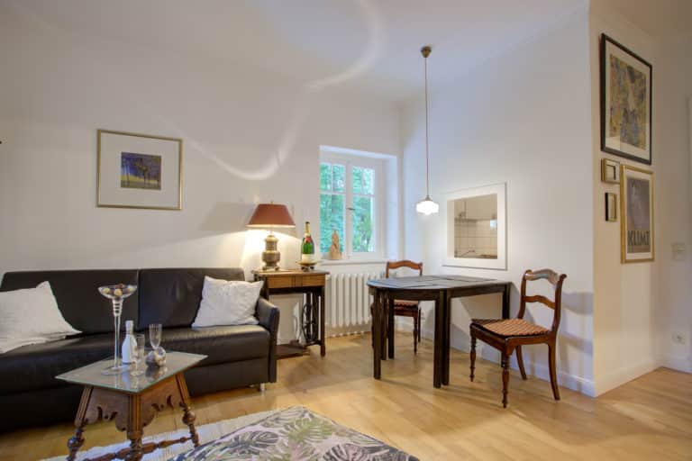 Haus_Hubertus_-32-3 – Hubertus Boltenhagen Wohnzimmer mit Ledersofa, Holztisch, Stühlen, Lampe und Fenster.