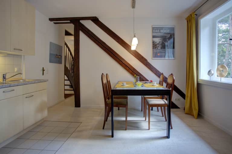 Haus_Hubertus_-42-4 – Hubertus Boltenhagen Esszimmer mit Holztisch, Stühlen und Treppe, hell erleuchtet.