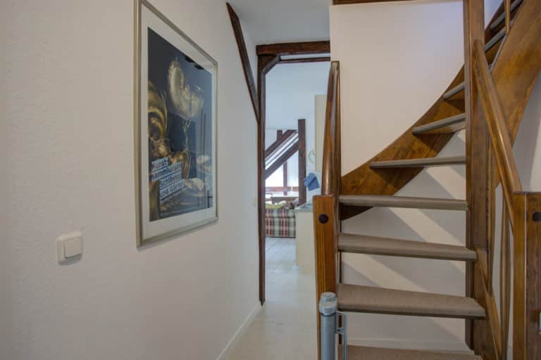 Haus_Hubertus_-62-9 – Hubertus Boltenhagen Treppenhaus mit Holzwendeltreppe und Gemälde an der weißen Wand.