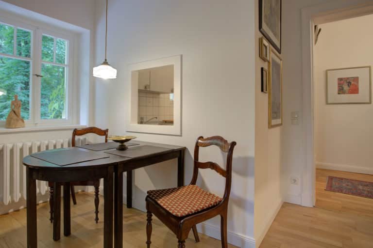 Haus_Hubertus_-7-21 – Hubertus Boltenhagen Essbereich mit dunklem Holztisch, zwei Stühlen, Wandbildern und Pendelleuchte.