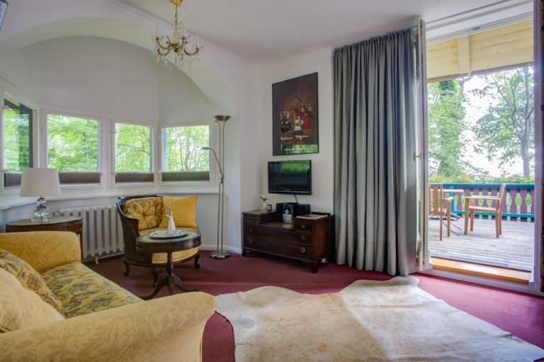 Haus_Hubertus_-7 – Hubertus Boltenhagen Gemütliches Wohnzimmer mit Sofa, Fernseher und Zugang zum Balkon.