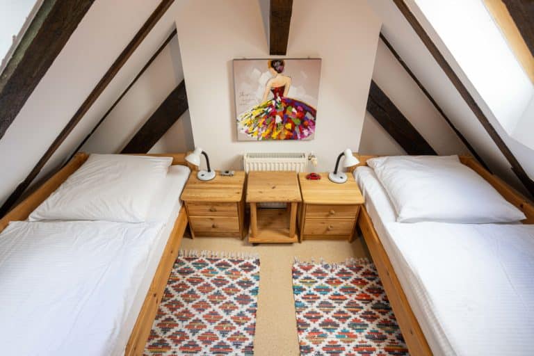 Haus_Hubertus_-7531-2 – Hubertus Boltenhagen Zwei Einzelbetten in einem Dachzimmer mit buntem Teppich und Wandbild.