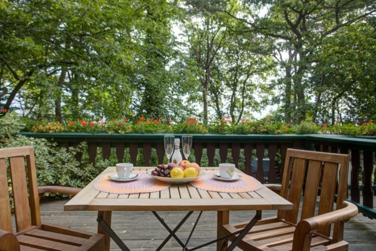 Haus_Hubertus_-82 – Hubertus Boltenhagen Holztisch auf Terrasse mit Obstschale, Tassen, vor grünem Gartenhintergrund.