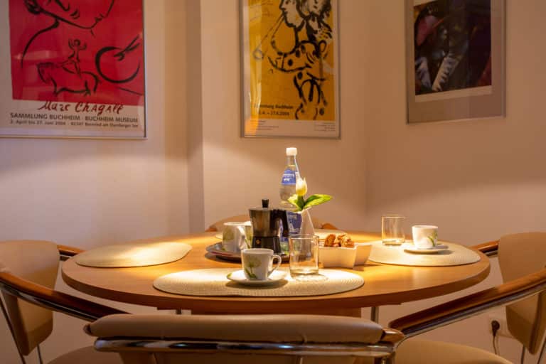 Hubertus1-0145 – Hubertus Boltenhagen Runder Tisch mit Kaffeeservice und Postern an der Wand.