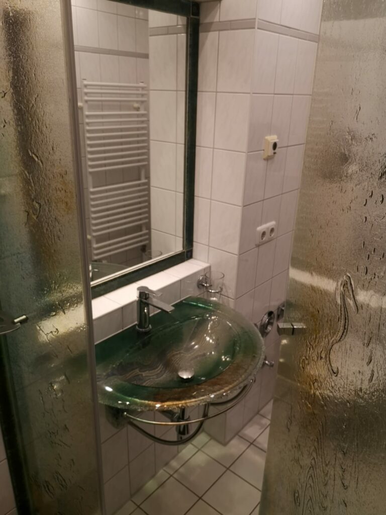 IMG-20251110-WA0014 – Hubertus Boltenhagen Modernes Badezimmer mit einem runden, grünen Waschbecken, Spiegel und gläserner Duschabtrennung.