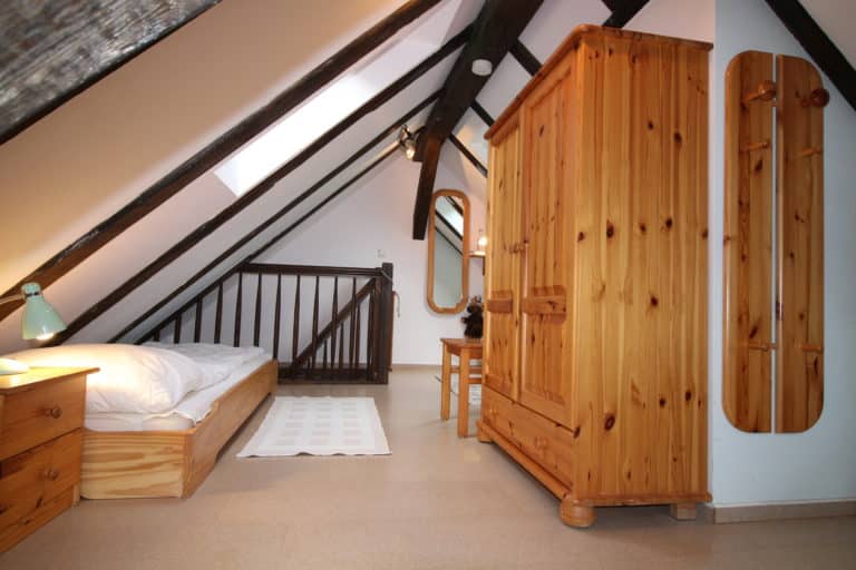 IMG_4762 – Hubertus Boltenhagen Dachzimmer mit Bett, Holzschrank und schrägen Deckenbalken.
