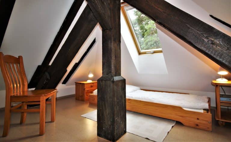 IMG_4772 (2) – Hubertus Boltenhagen Dachzimmer mit Holzbalken, Einzelbett und Fenster mit Blick ins Grüne.