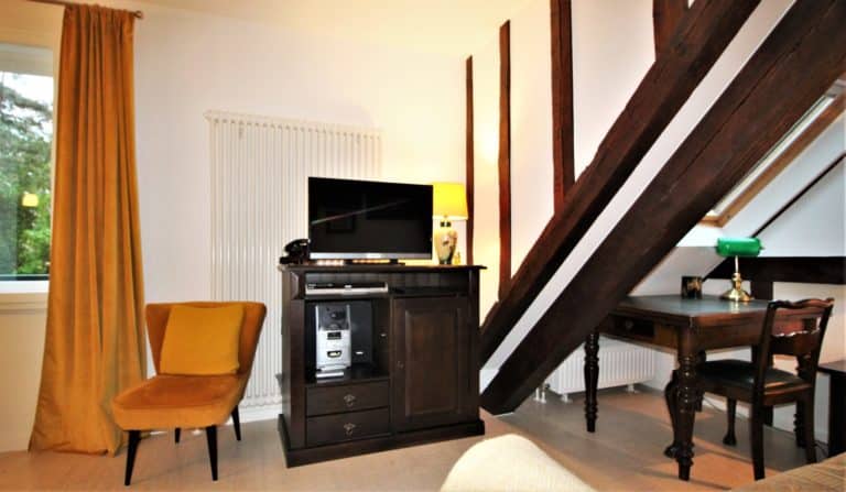 IMG_6156 (2) – Hubertus Boltenhagen Schrank mit TV und Lampe, gelber Sessel, schräge Holzstreben.