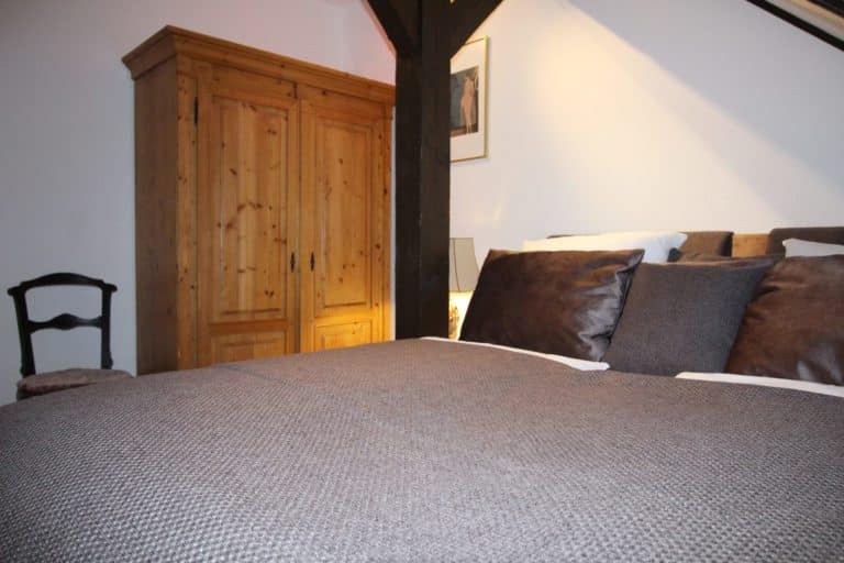 IMG_6221 (2) – Hubertus Boltenhagen Holzschrank und gemütliches Bett mit braunen Kissen in hellem Zimmer.