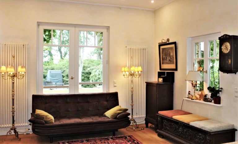 IMG_6534 (2) – Hubertus Boltenhagen Helles Wohnzimmer mit braunem Sofa, Lampen und Gartenausblick.