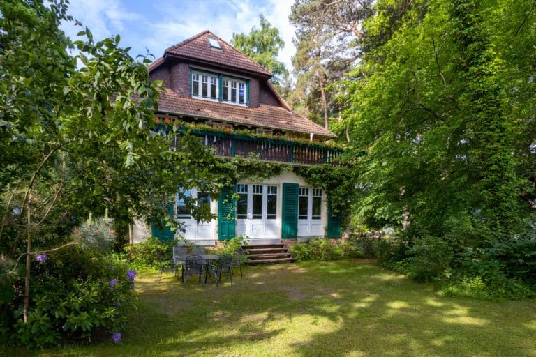 HausHubertus_Aussen-0884 – Hubertus Boltenhagen House with red roof and ivy, surrounded by a lush garden.