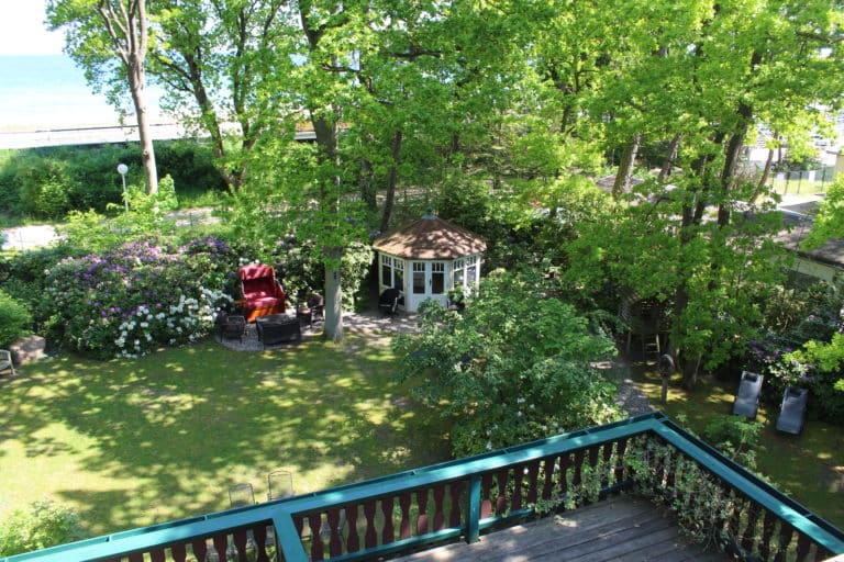 IMG_5290 – Hubertus Boltenhagen Green garden with pavilion and red chairs, surrounded by trees.