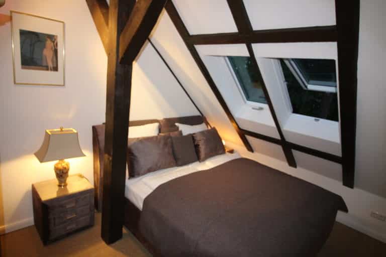 IMG_6232 – Hubertus Boltenhagen Cozy bedroom under the roof with dark wooden beams and a double bed.
