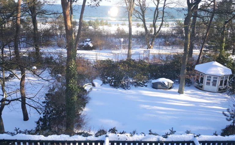 20180228_092823 (2) – Hubertus Boltenhagen Snow-covered garden with trees and the sunlit sea behind.